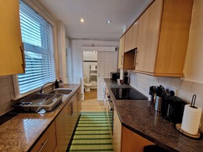 A kitchen with granite countertops, wooden cabinets, a built-in oven, and a window with blinds. - Luxurious & Cosy Home w/ Free Parking and Garden (Coventry)