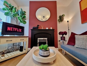 A living room with a flat-screen TV, a fireplace, a sofa, and a coffee table with a plant. - Luxurious & Cosy Home w/ Free Parking and Garden (Coventry)