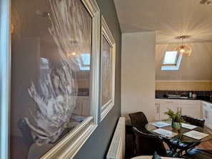 A modern dining area with a glass table, chairs, and a view of the kitchen. - Trendy Condo Near City Centre w/ Free Parking (Coventry)