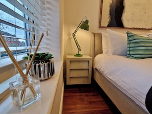 A bedroom with a bed, bedside table, lamp, and window with blinds. - Trendy Condo Near City Centre w/ Free Parking (Coventry)