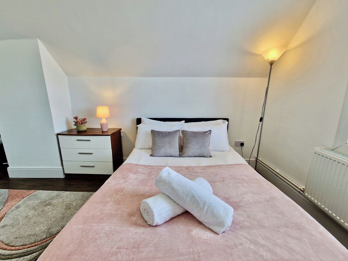 Habitación de hotel con cama, mesita de noche, lámpara y una toalla enrollada sobre la cama.