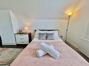Een hotelkamer met een bed, nachtkastje, lamp en een opgerolde handdoek op het bed.