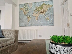 Ein Wohnzimmer mit einer großen Weltkarte an der Wand, einem Sofa, einem Couchtisch und einer Topfpflanze.