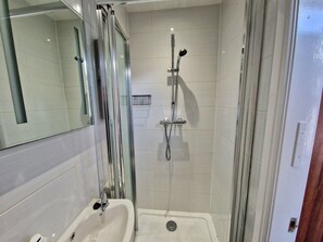 Un baño con ducha de vidrio, lavamanos y espejo.