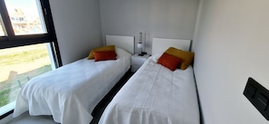 A hotel room with two beds, each with a white bedspread and a red and yellow pillow. There is a nightstand with a lamp between the beds. - Penthouse Innovabeach Punta Prima (Orihuela)