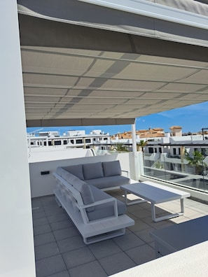 A rooftop terrace with a white sofa, a small table, and a pergola providing shade. - Penthouse Innovabeach Punta Prima (Orihuela)