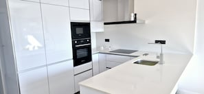 A modern kitchen with white cabinetry, a built-in oven, a countertop with a sink, and a black range hood. - Penthouse Innovabeach Punta Prima (Orihuela)