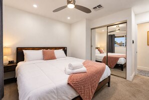 Ein Hotelzimmer mit einem Bett, einem Nachttisch, einem Deckenventilator, einem Spiegel und Blick durch das Fenster.