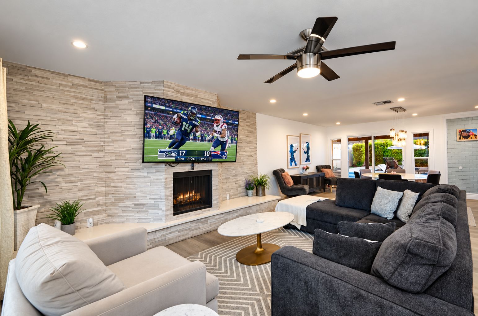 A modern living room with a flat-screen TV, a fireplace, and a ceiling fan.