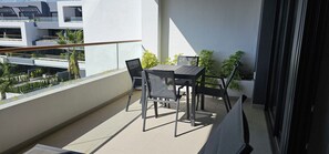 A balcony with a table and chairs, potted plants, and a view of a modern building. - Lagoons Village Tm Torrevieja (Torrevieja)