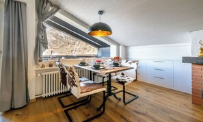 Ein Essbereich mit Tisch, Stühlen, einem Heizkörper, einem Fenster mit Vorhängen und einer Hängelampe.