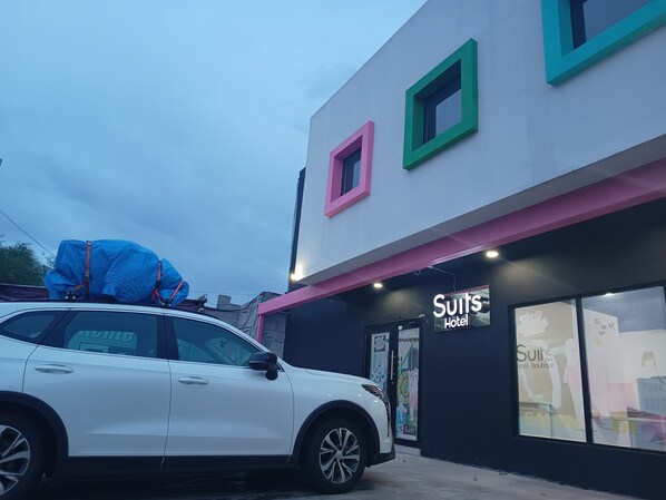 A white car parked in front of a building with a sign that reads 'Suits Hotel Boutique.'