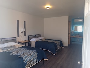 A room with two beds, a bedside table, a wall-mounted phone, and a bathroom with a sink and mirror. - New Listing (Nuevo Casas Grandes)