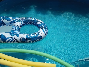 Et klart, blåt pool med en blå og hvid oppustelig ring og to grønne og gule poolnudler.