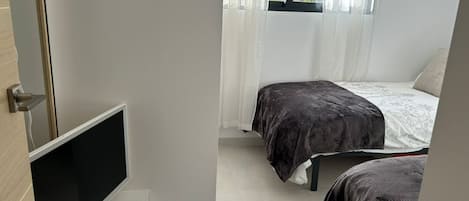 A bedroom with a bed, a TV, and a window with curtains.