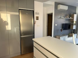 Una cocina moderna con refrigerador de acero inoxidable, armarios blancos y un equipo de aire acondicionado empotrado.