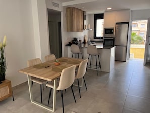 Una cocina moderna con una isla central, un comedor con mesa y sillas de madera, y vista a un edificio residencial.