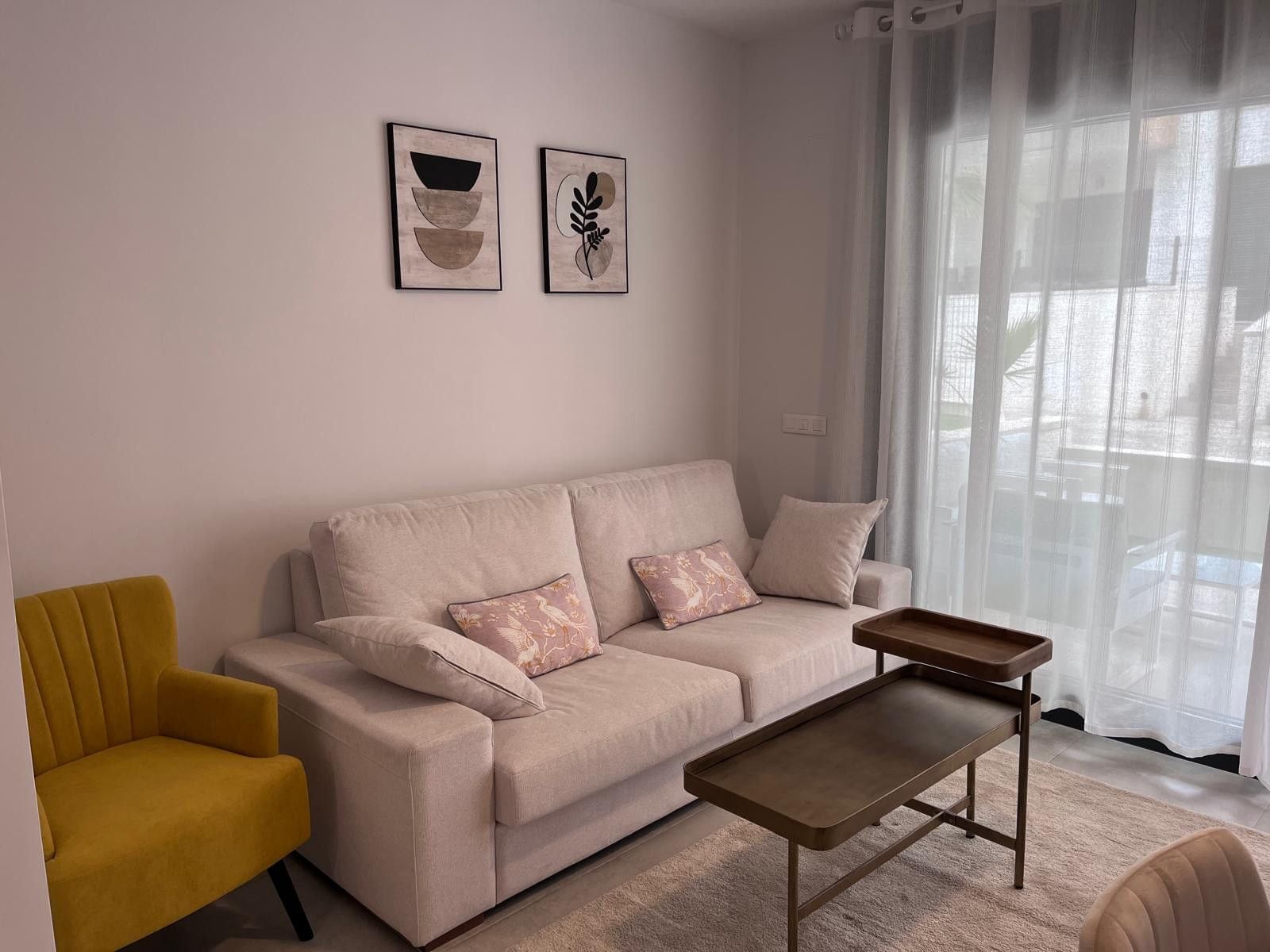 A living room with a sofa, a yellow armchair, a coffee table, and two wall-mounted artworks.