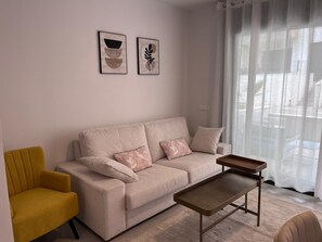 Een woonkamer met een bank, een gele fauteuil, een salontafel en twee kunstwerken aan de muur.