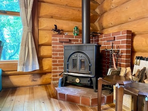 A log cabin interior with a brick fireplace, wooden walls, and a window with a curtain. - New Listing (皆野町)