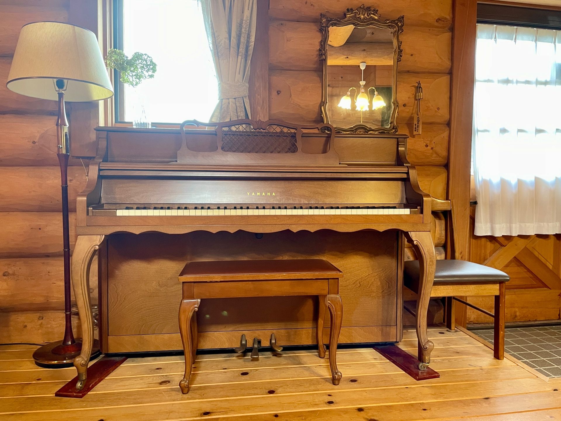 A wooden interior with a grand piano, a small table, a chair, and a lamp.