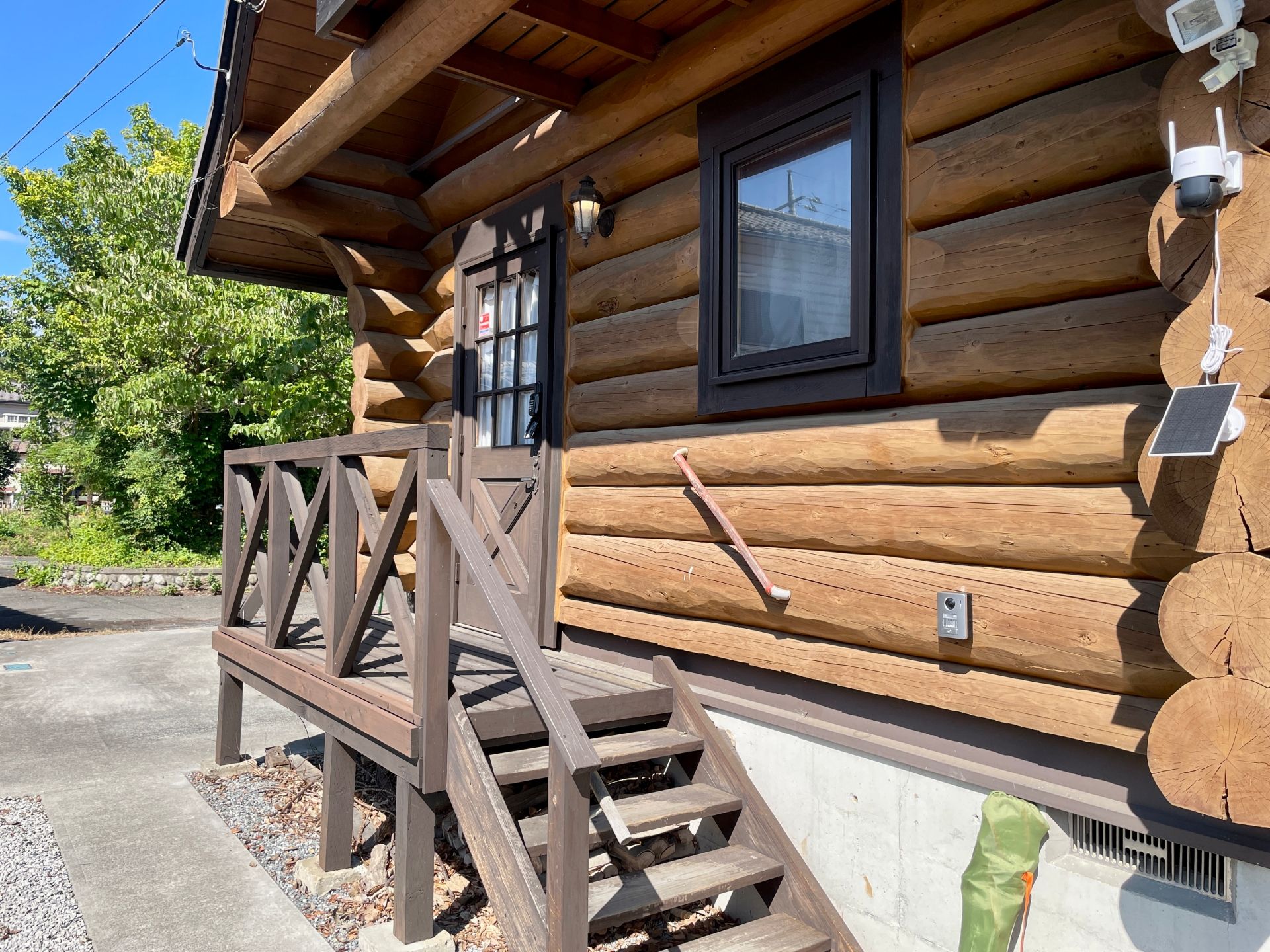 A log cabin with a wooden staircase leading to a door, a window, and a solar panel on the side.
