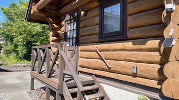 A log cabin with a wooden staircase leading to a door, a window, and a solar panel on the side.
