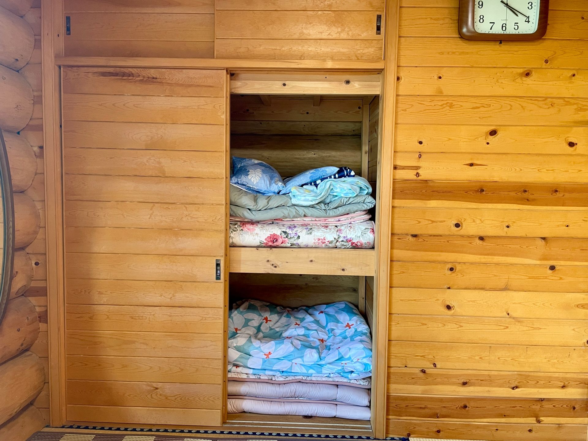A wooden interior with a double door leading to a storage area containing folded bedding.
