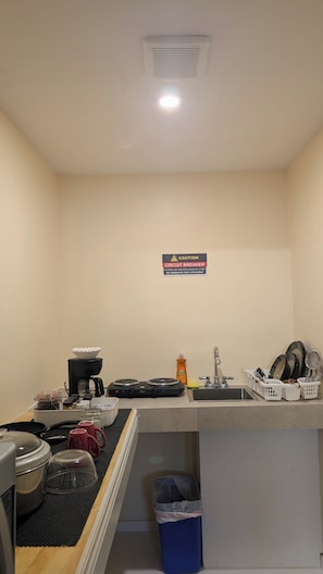 Uma cozinha compacta equipada com cafeteira, fogão, pia e lixeira.