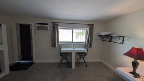 A small room with a window, a table with two chairs, a hanging shelf, and a lamp. - Howard Motel (Windsor)