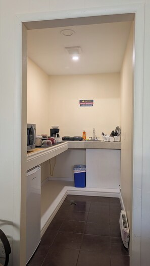 A compact kitchen with a microwave, stove, sink, and a trash bin. - Howard Motel (Windsor)