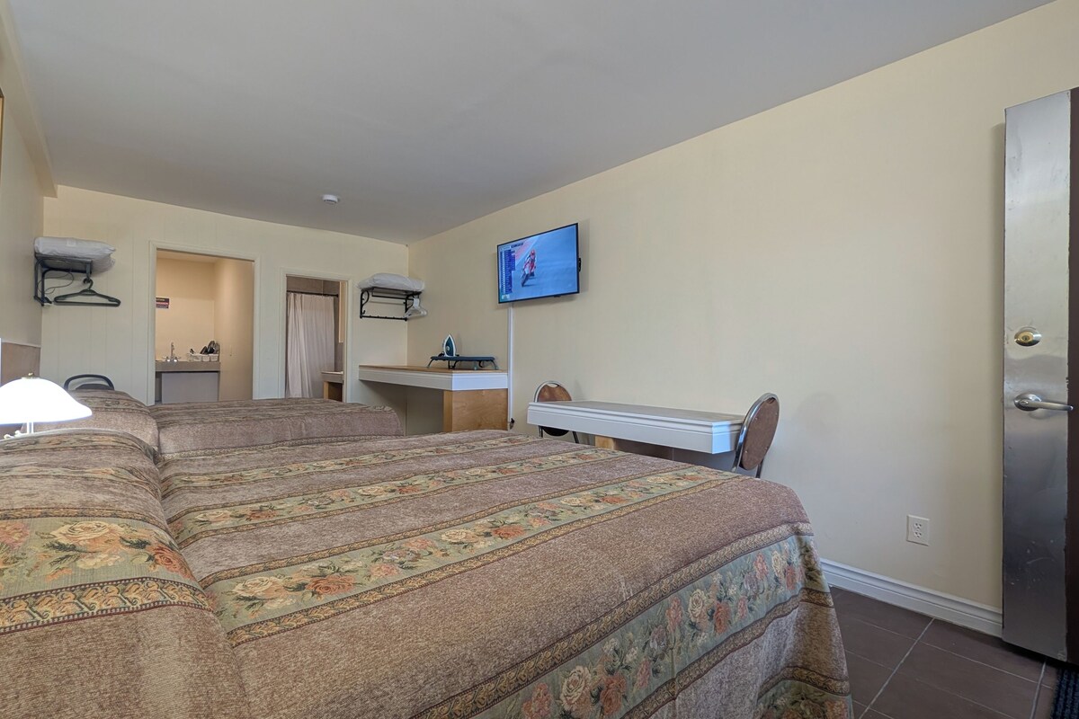 Quarto de hotel com cama grande, escrivaninha, televisão e banheiro visível por uma porta aberta.