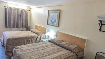 Quarto de hotel com duas camas, uma mesa de cabeceira, uma cadeira, um quadro na parede e uma luminária no teto.
