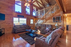 A log cabin interior with a staircase, wooden floors, a sofa, and a coffee table. - Comfy 4-bedroom cabin with picturesque views, near Pigeon Forge and Gatlinburg (Sevierville)