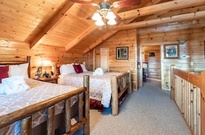 Une cabine avec deux lits en bois, un ventilateur de plafond et un couloir menant à une autre pièce.