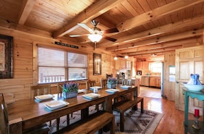A wooden cabin interior with a dining table set for four, a ceiling fan, and a kitchen area visible through an open door. - Comfy 4-bedroom cabin with picturesque views, near Pigeon Forge and Gatlinburg (Sevierville)