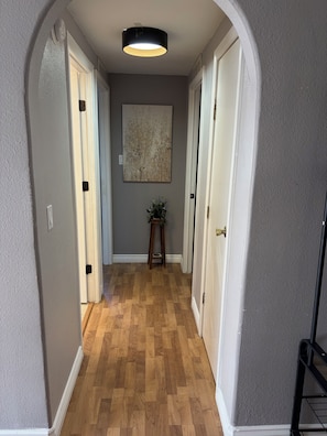 A hallway with wooden flooring, white doors, a ceiling light, and a wall-mounted artwork. - 3-bedroom, King bed in spacious condo (Wildomar)