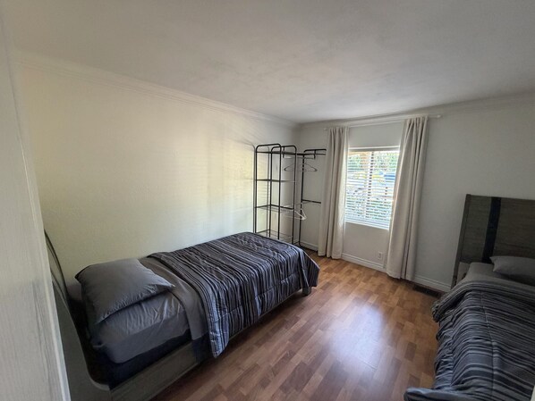 A small, single-room accommodation with a wooden floor, a bed with a striped bedspread, a metal wardrobe, and a window with curtains. - 3-bedroom, King bed in spacious condo (Wildomar)