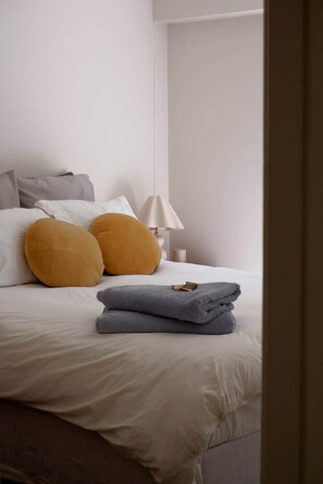 Ein ordentlich bezogenes Bett mit Kissen, einer zusammengelegten Decke und einer Lampe auf einem Nachttisch.