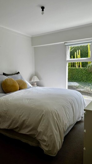Quarto com cama, mesa de cabeceira, luminária e janela com vista para cactos.