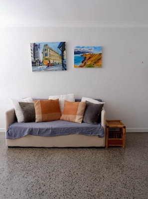 Ein Zimmer mit einem beigen Sofa, einer blauen Decke und einer kleinen Holzkiste.