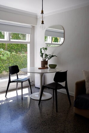 Uma área de refeições com uma mesa redonda, duas cadeiras, uma planta em vaso, uma tigela e um espelho na parede.