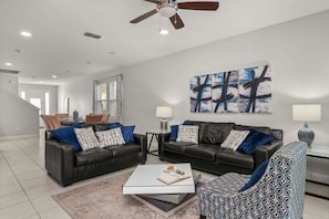 A modern living room with two leather sofas, a patterned armchair, a coffee table, and a ceiling fan. - 6BR Group Escape w/ Private Pool, Spa & Games (Kissimmee)