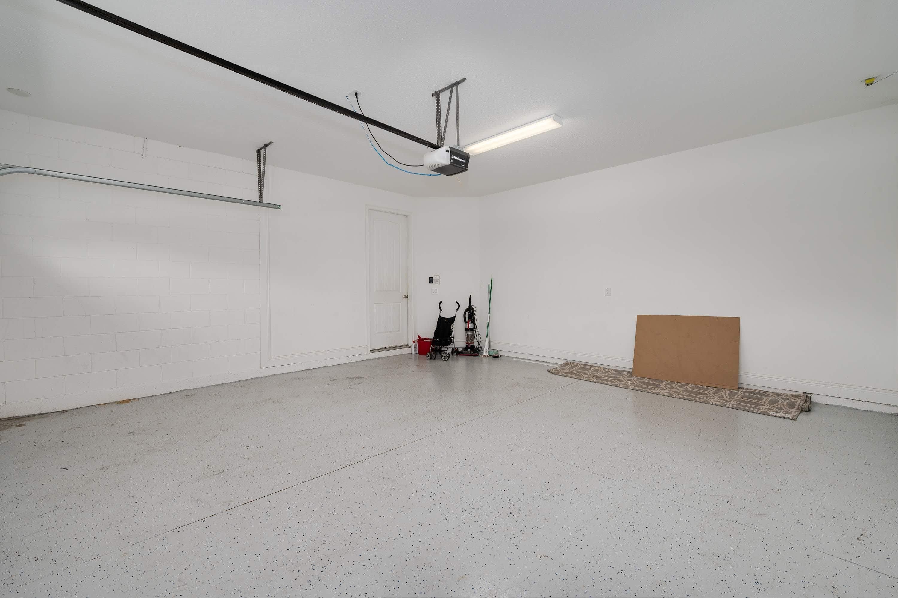 A spacious, empty room with a concrete floor, a white door, and a ceiling-mounted light fixture.