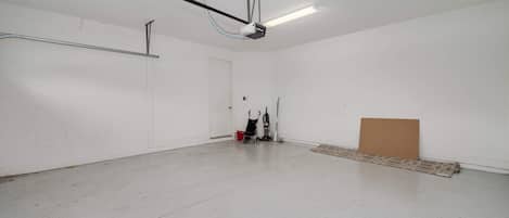 A spacious, empty room with a concrete floor, a white door, and a ceiling-mounted light fixture.
