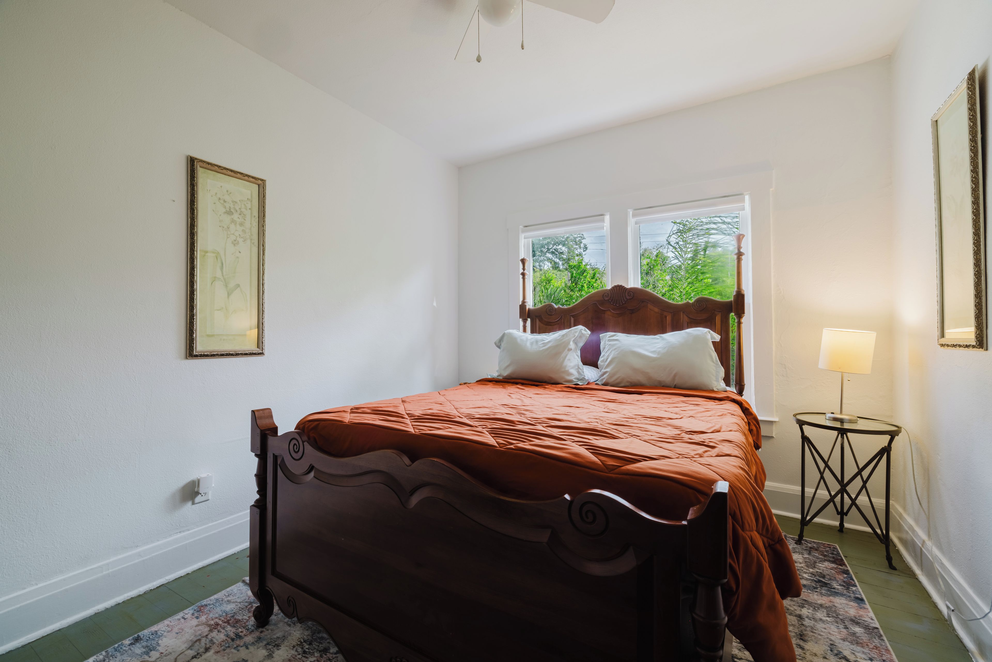 Une chambre à coucher avec un lit en bois, une table de chevet avec une lampe et une fenêtre donnant sur un paysage verdoyant.