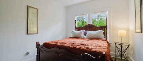 Ein Schlafzimmer mit einem hölzernen Bett, einem Nachttisch mit Lampe und einem Fenster mit Blick ins Grüne.