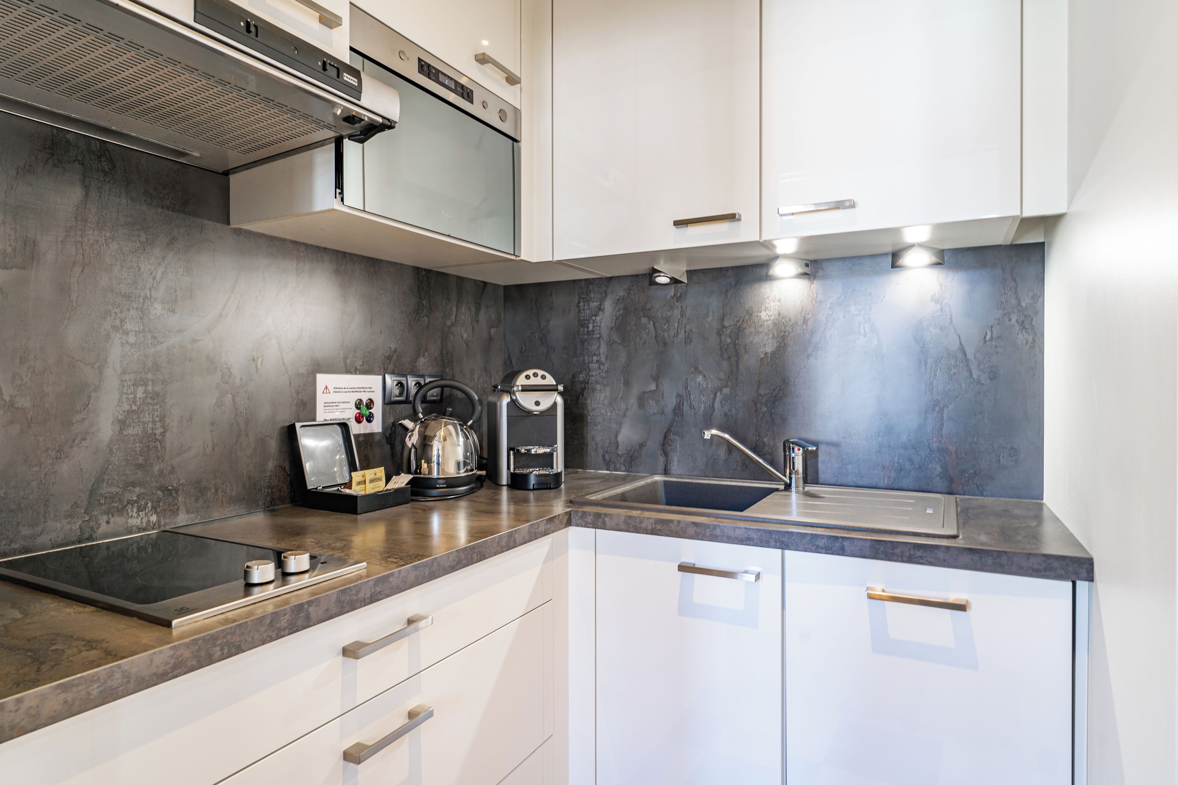 A modern kitchen with a built-in espresso machine, a kettle, and a sink.