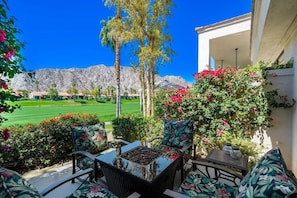 Eine Terrasse mit Gartenmöbeln, einer Feuerstelle und Blick auf einen Golfplatz und Berge.