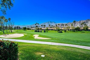 Ein Golfplatz mit blauem Himmel, Palmen und einem Berg im Hintergrund.